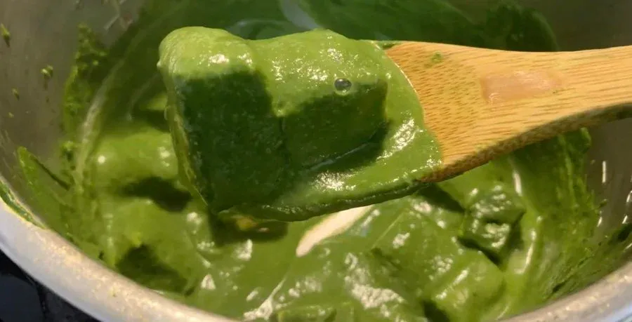 Creamy green palak paneer being stirred in a pot with a wooden spoon, showing the soft cheese cubes in spinach sauce.