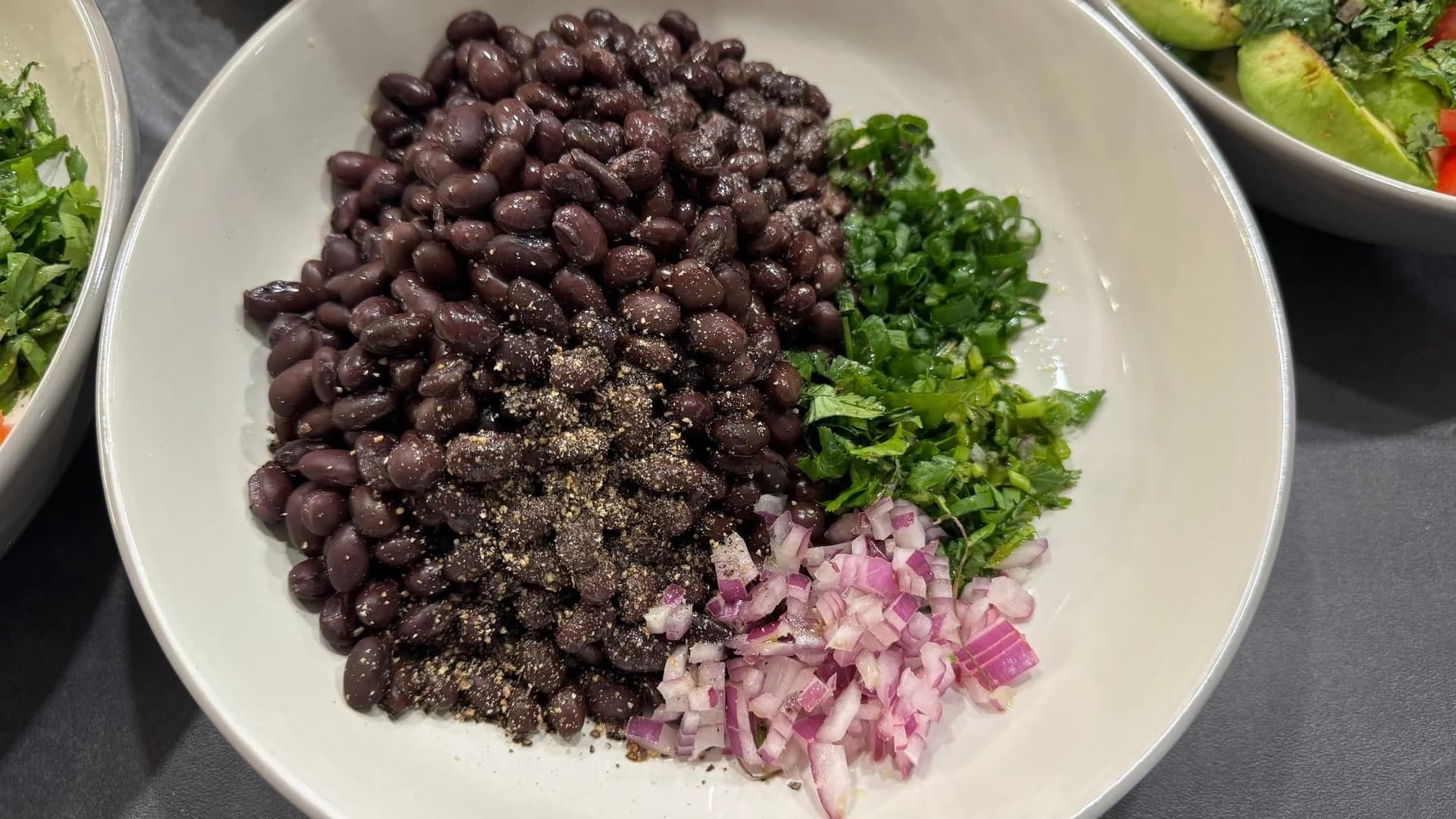 White bowl with black beans, fresh cilantro, diced red onion, and seasoning for black bean salsa.