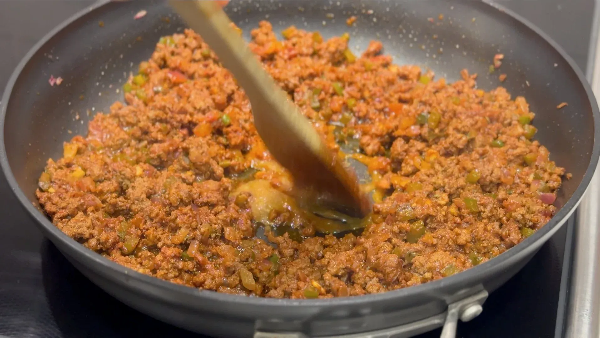 Ground meat mixture with vegetables being stirred in a skillet for Belizean meat pie filling.