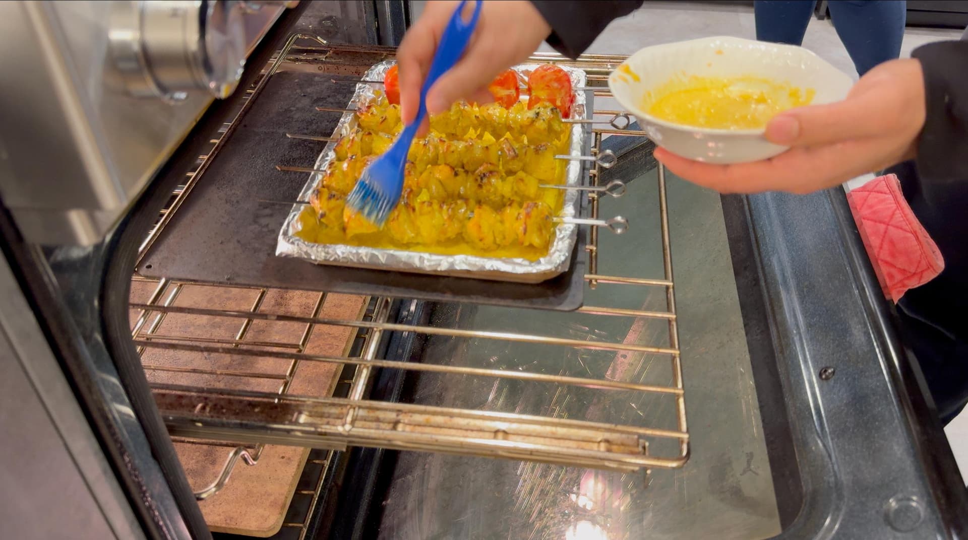 Brushing yellow saffron rice onto oven-broiled chicken skewers in a baking pan during cooking.