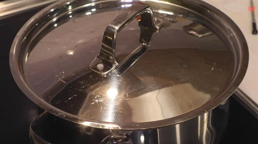Milk separating into curds and whey in a pot with a glass lid during paneer making.