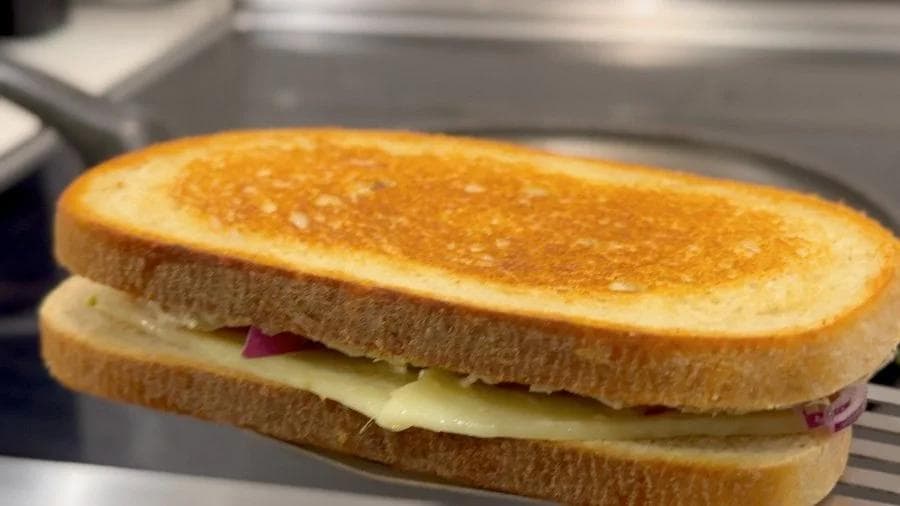 Golden brown toasted tuna melt sandwich with melted cheese and red onion visible between two slices of bread.