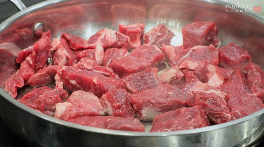 Raw beef cubes being seared in a stainless steel pan over high heat for Balinese beef rendang.