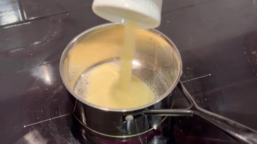 Condensed milk being poured into a saucepan of whole milk mixture for making kheer ice cream.