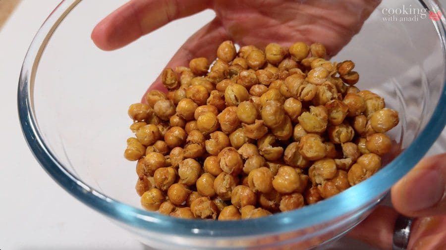 Crispy roasted chickpeas in a clear glass bowl being held in someone's hands.