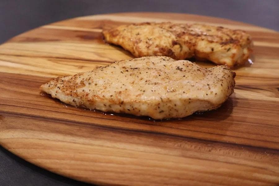 Two seasoned air fryer chicken breasts on a wooden cutting board, golden-brown and peppered.