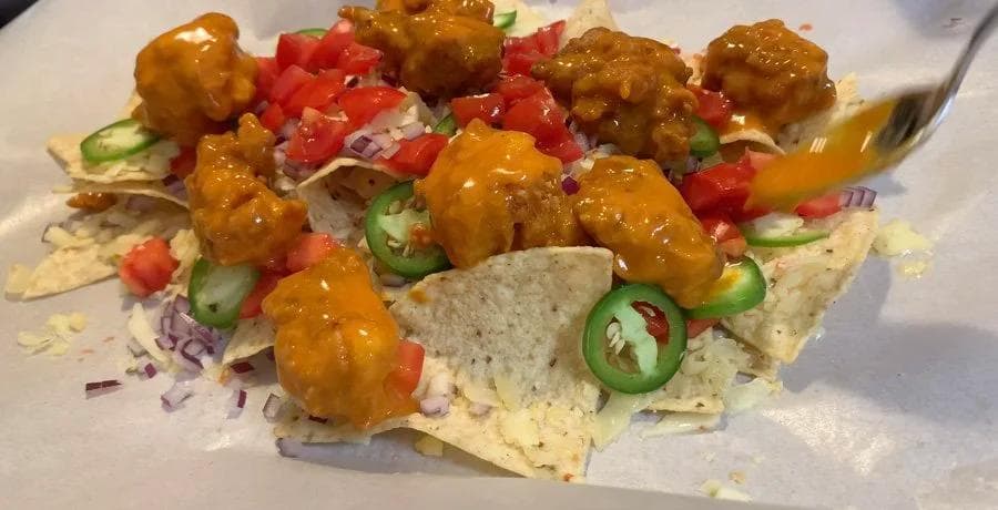 Buffalo chicken nachos topped with melted cheese, diced tomatoes, jalapeños, and red onions on tortilla chips.