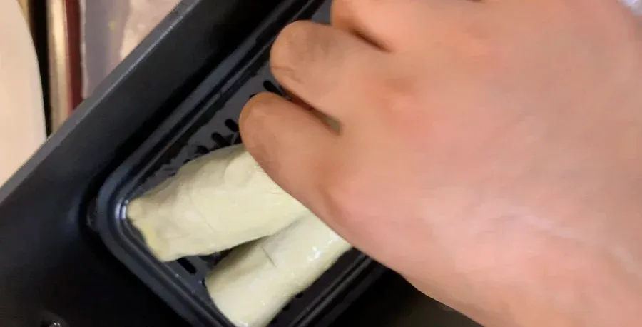 Hand brushing egg wash onto chilled sausage roll pastry in a dark baking tray.
