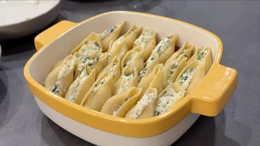 Jumbo pasta shells filled with ricotta cheese mixture arranged in a yellow and white baking dish.